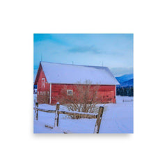 Red barn surrounded by snow with mountains in the background, featured on a matte-finish poster with giclée printing quality.