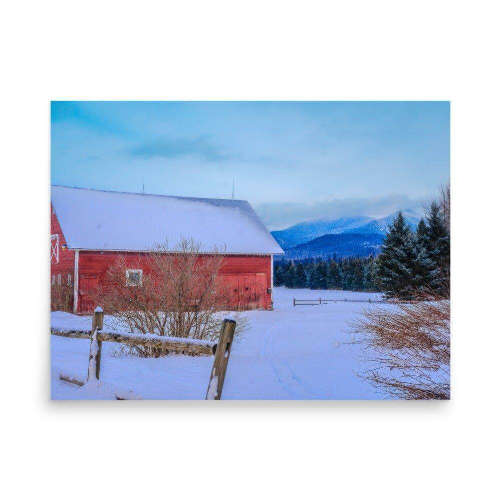 Red barn in a snowy mountain landscape with pine trees and a clear blue sky.